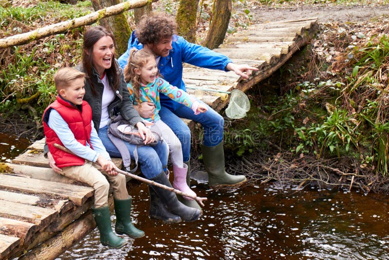 Family Sitting On Bridge Fishing In Pond With Net