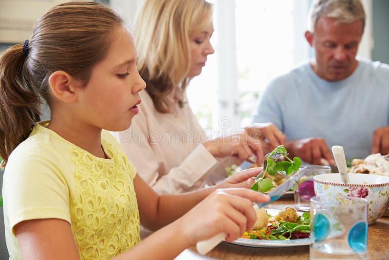 Family Sitting At Table Enjoying Meal At Home Together