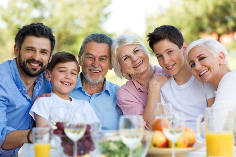 Family Sitting at Table Outdoors, Smiling Stock Photo - Image of ...