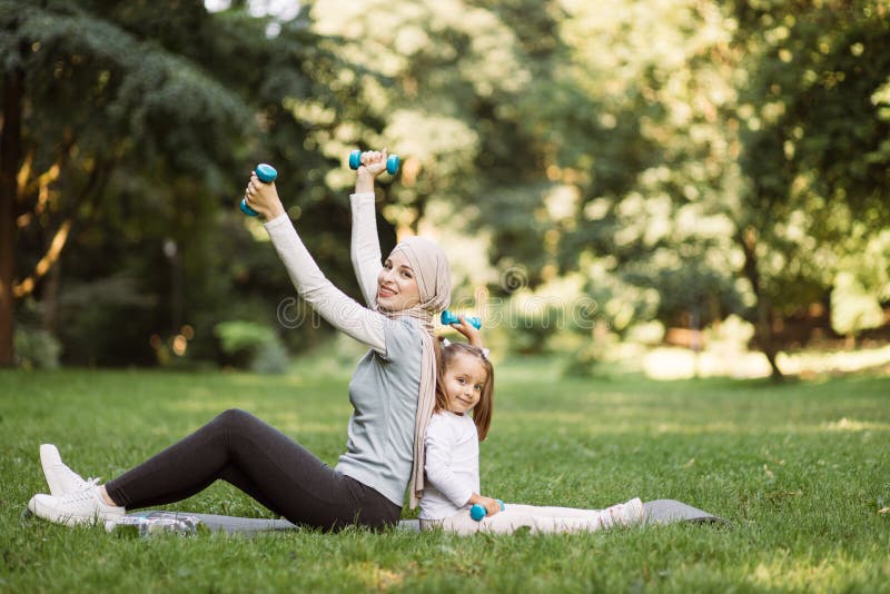 Muslim Arabian woman working out with dumbbells together with her daughter in the park