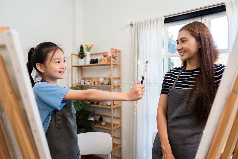 Family time as a girl shares a paintbrush with her mom stock images