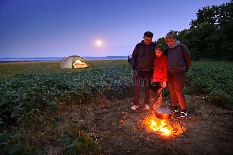 Family traveling and camping, twilight, cooking on the fire. Beautiful nature - field, forest, stars and moon royalty free stock photos Family traveling and camping, twilight, cooking on the fire. Beautiful nature - field, forest, stars and moon royalty free stock photos