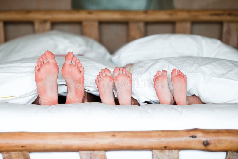 Family with two kids laying in bed with their feet forward.