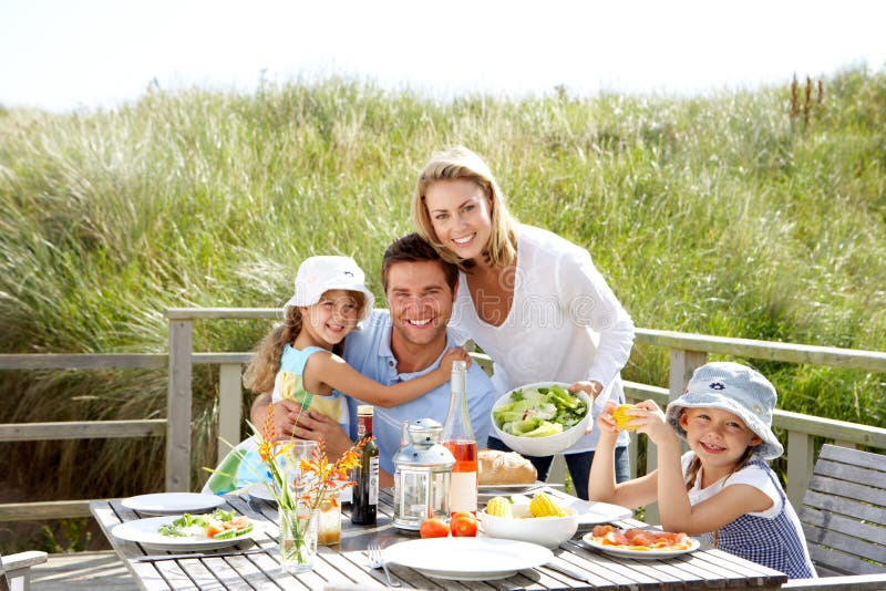 La famiglia in vacanza a mangiare il pranzo all'aperto e sorridente alla macchina fotografica.