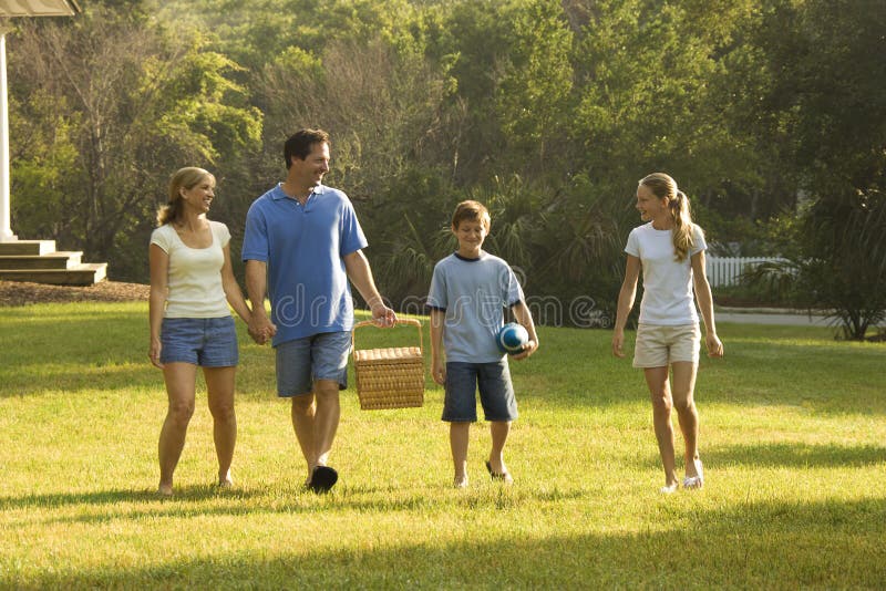 Caucasica famiglia di quattro persone a piedi nel parco portando cestino da picnic.