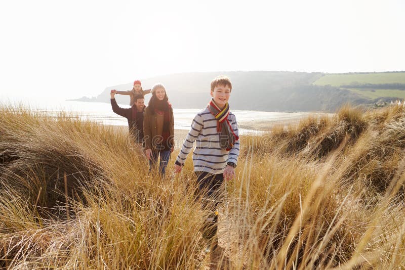 Family Walking Through Sand Dunes On Winter Beach