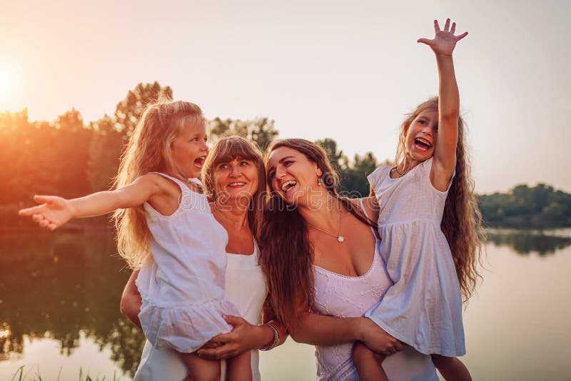Family walking by summer river at sunset. Mother and grandmother holding kids and laughing. Three denerations royalty free stock image Family walking by summer river at sunset. Mother and grandmother holding kids and laughing. Three denerations royalty free stock image