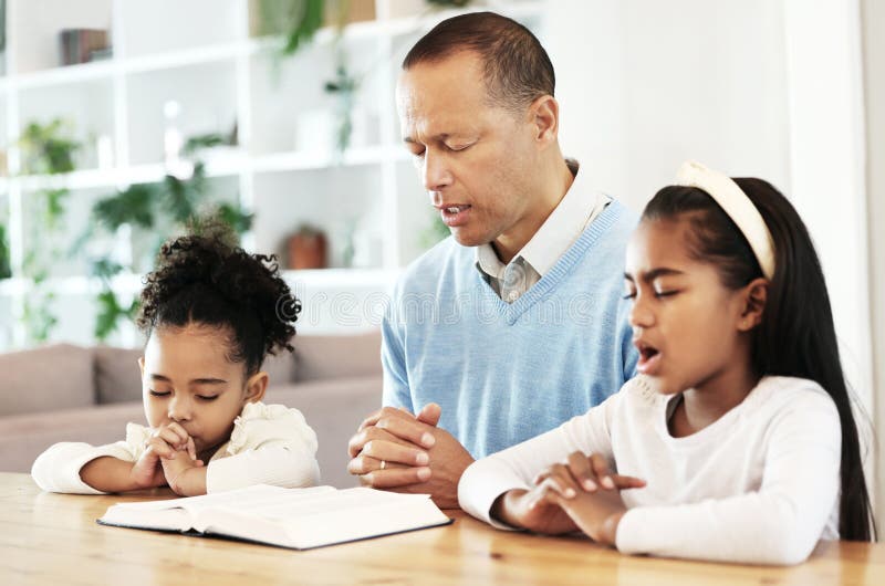 Family, worship and bible with father and kids praying at table for peace, religion and faith in their home. God, pray