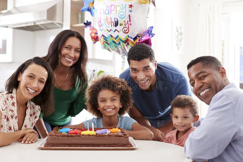 Família afro-americano da família de três gerações recolhida na cozinha que comemora um aniversário junto, olhando ao smilin da c
