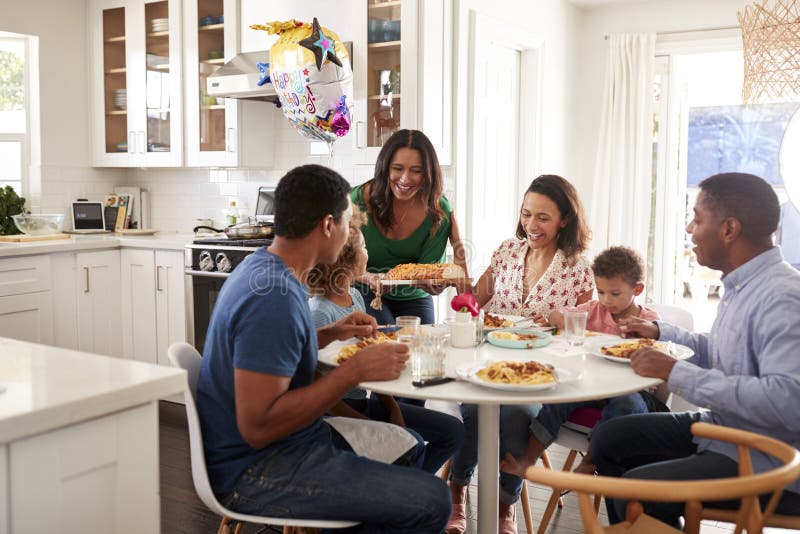 Família afro-americano de três gerações que senta-se junto na mesa de cozinha, com a avó que serve o alimento