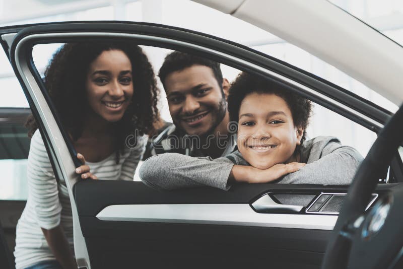 African american family at car dealership. Mother, father and son are pising in window of new grey car. African american family at car dealership. Mother, father and son are pising in window of new grey car.