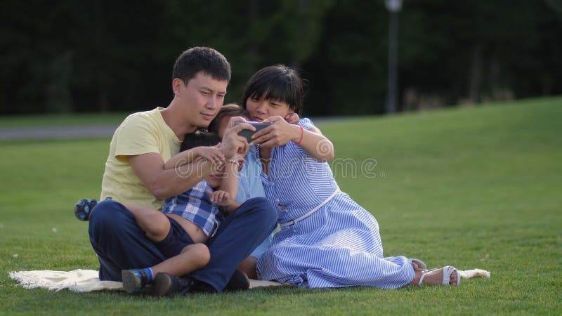 Família asiática alegre com as crianças que tomam o selfie no parque