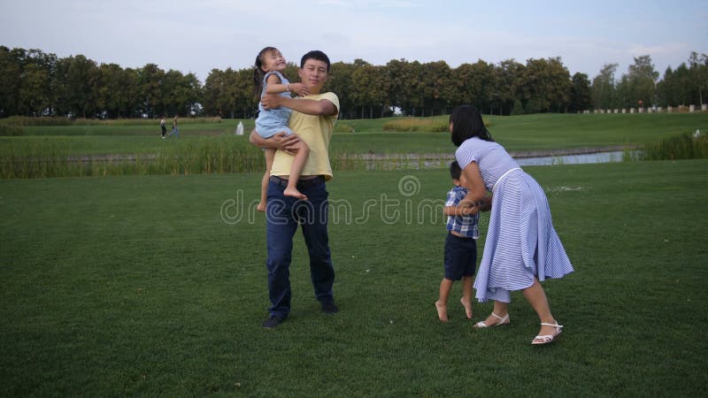 Família asiática alegre que anda guardando as mãos no parque
