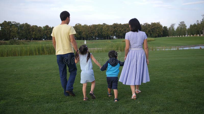 Família asiática que guarda as mãos e que anda fora