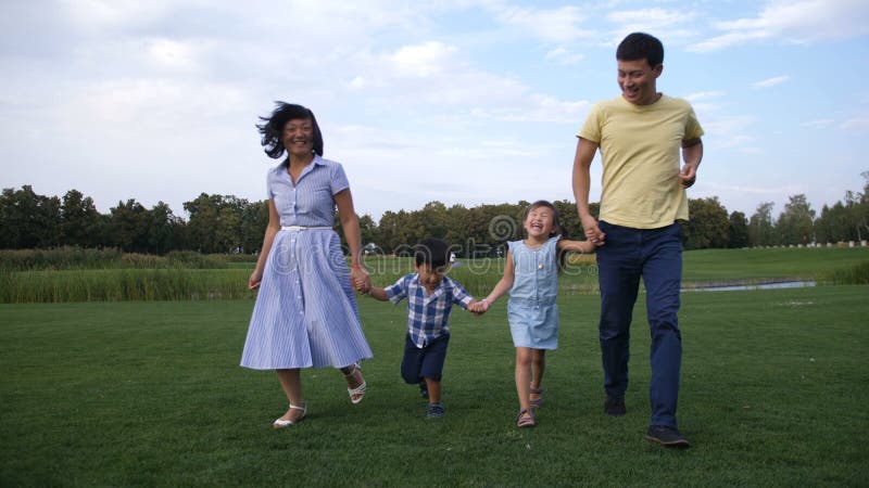 Família asiática que guarda as mãos e o corredor no parque