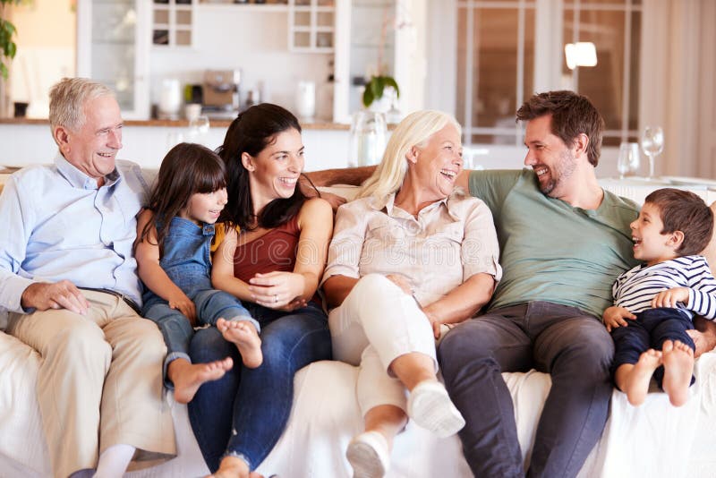 Família branca feliz de três gerações que senta-se em um sofá em casa que olha se, vista dianteira foto de stock Família branca feliz de três gerações que senta-se em um sofá em casa que olha se, vista dianteira foto de stock
