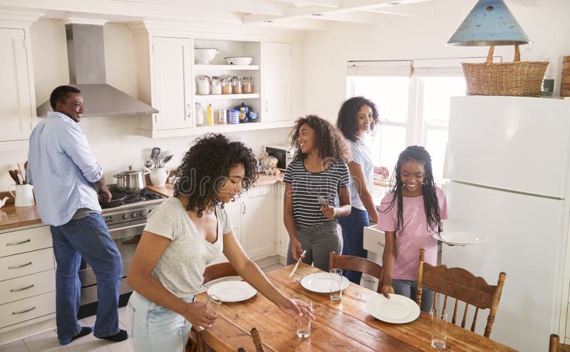 Família com as filhas adolescentes que colocam a tabela para a refeição na cozinha