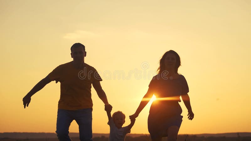 Família correndo no parque. mãe e pai correm com o bebê na silhueta da natureza segurando as mãos jogando