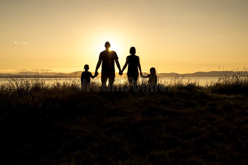 Família de quatro pessoas no preto da sombra do por do sol backlit