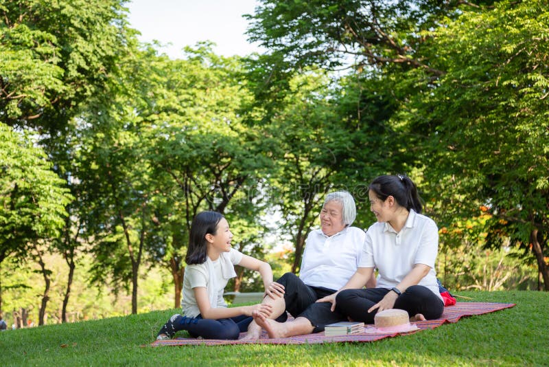 A família de sorriso feliz que senta-se na esteira no parque exterior, avó superior asiática que recebe a massagem pela neta, rel foto de stock A família de sorriso feliz que senta-se na esteira no parque exterior, avó superior asiática que recebe a massagem pela neta, rel foto de stock