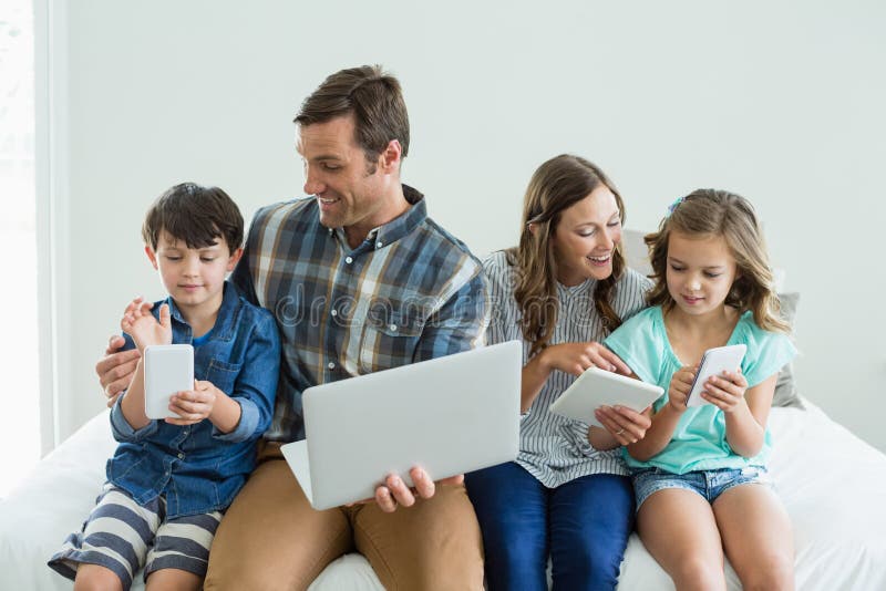 Família de sorriso que usa o portátil, a tabuleta digital e o telefone celular no quarto imagens de stock royalty free Família de sorriso que usa o portátil, a tabuleta digital e o telefone celular no quarto imagens de stock royalty free