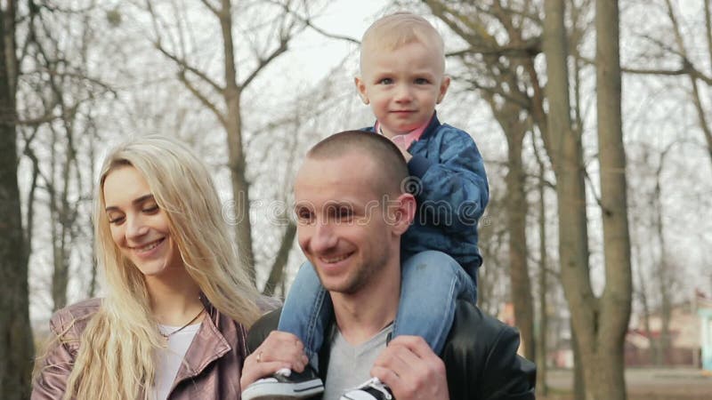 Família de três feliz que anda na primavera parque