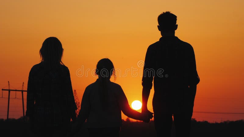 Família de três que admira o por do sol alaranjado sobre a cidade, vista traseira foto de stock Família de três que admira o por do sol alaranjado sobre a cidade, vista traseira foto de stock