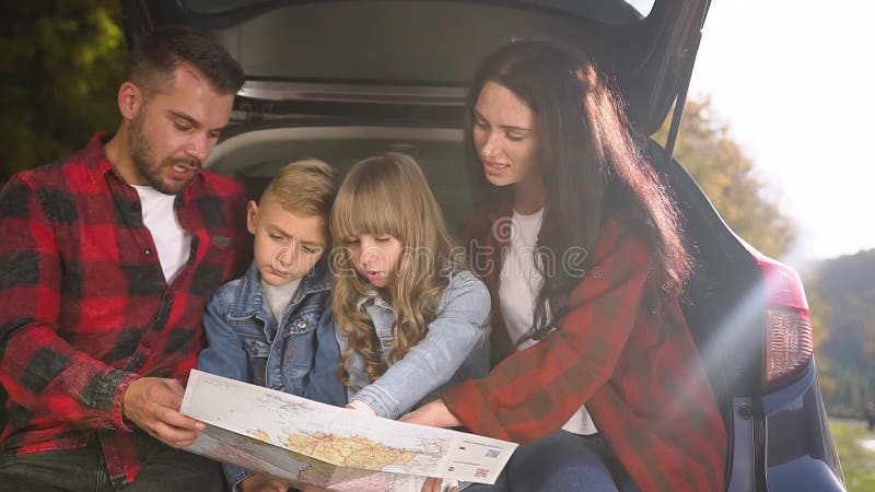 Família divertida atrativa sentada no porta-malas e olhando no roteiro antes da viagem de carro