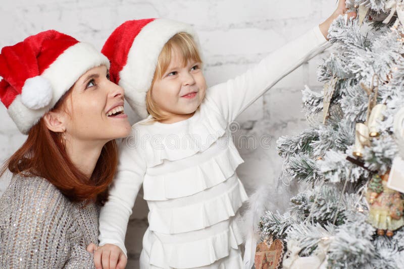 The pretty girl with mum are decorating a Christmas tree in the house. Happy family. The pretty girl with mum are decorating a Christmas tree in the house. Happy family.