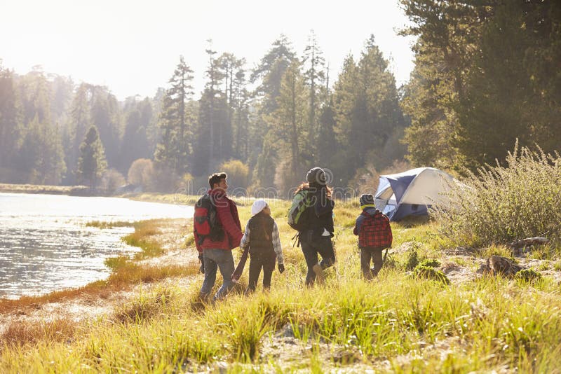 Família em uma viagem de acampamento que anda perto de um lago, vista traseira