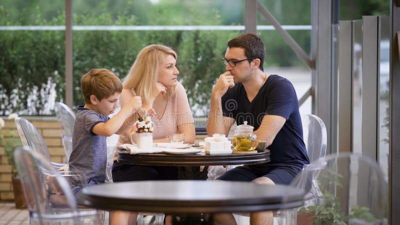 Família feliz com o filho que passa o tempo junto no terraço exterior Esposa e marido que falam quando menino que come a sobremes