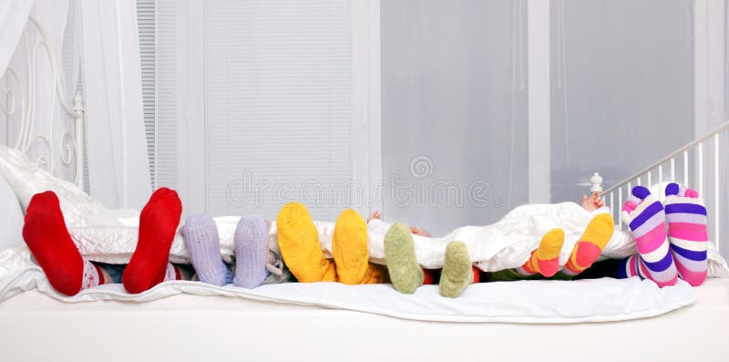 Família feliz em peúgas coloridas na cama branca.