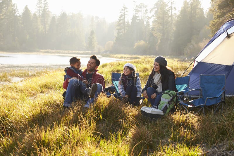 Família feliz em uma viagem de acampamento que relaxa por sua barraca imagem de stock Família feliz em uma viagem de acampamento que relaxa por sua barraca imagem de stock
