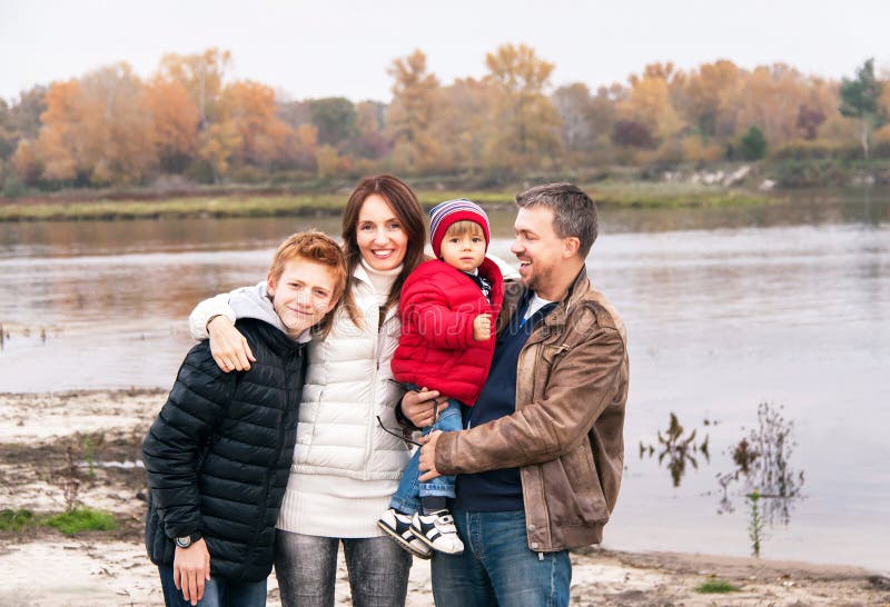A família feliz está estando perto do rio no dia do outono imagens de stock A família feliz está estando perto do rio no dia do outono imagens de stock