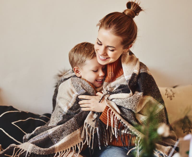 Família feliz, mãe e filho amável, abraço e gargalhada embrulhados num cobertor quente numa noite de inverno aconchegante