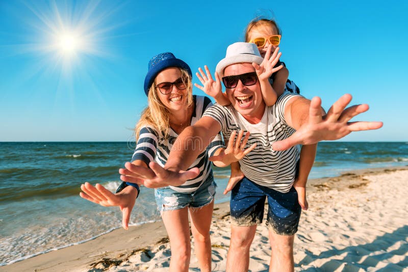 Família feliz na praia Povos que têm o divertimento em férias de verão Pai, mãe e criança contra o mar e o fundo azuis do céu