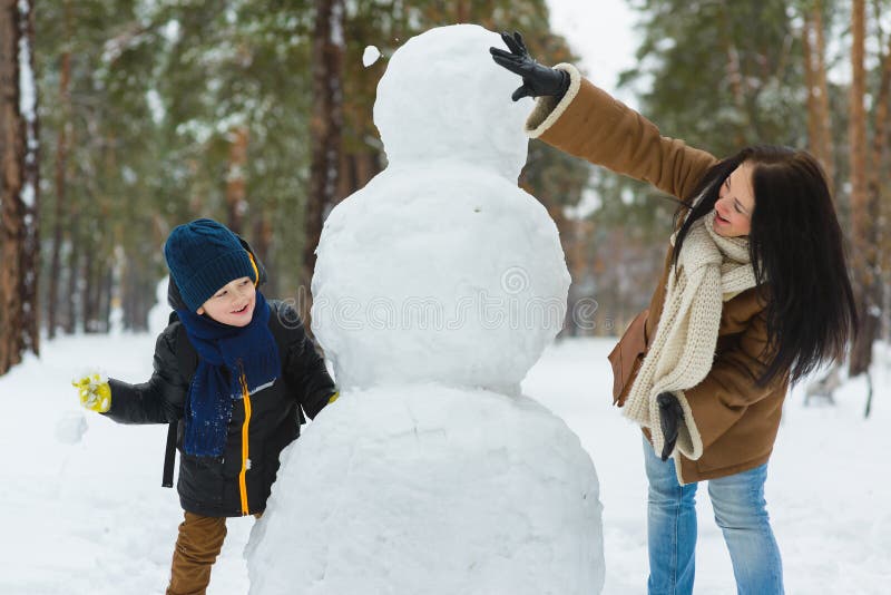 Família feliz na roupa morna Bolas de neve de sorriso do jogo da mãe e do filho ao lado de um boneco de neve exterior O conceito imagem de stock Família feliz na roupa morna Bolas de neve de sorriso do jogo da mãe e do filho ao lado de um boneco de neve exterior O conceito imagem de stock