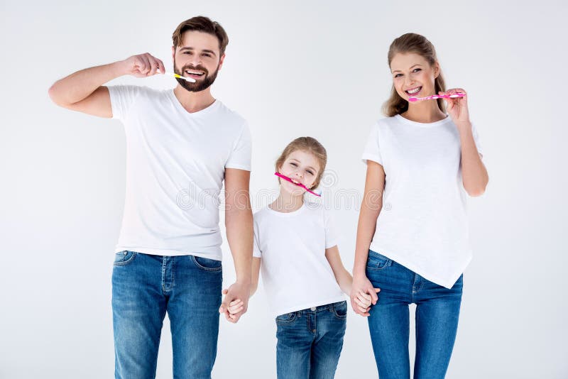 Família feliz nos t-shirt brancos que limpam os dentes com as escovas de dentes imagem de stock Família feliz nos t-shirt brancos que limpam os dentes com as escovas de dentes imagem de stock