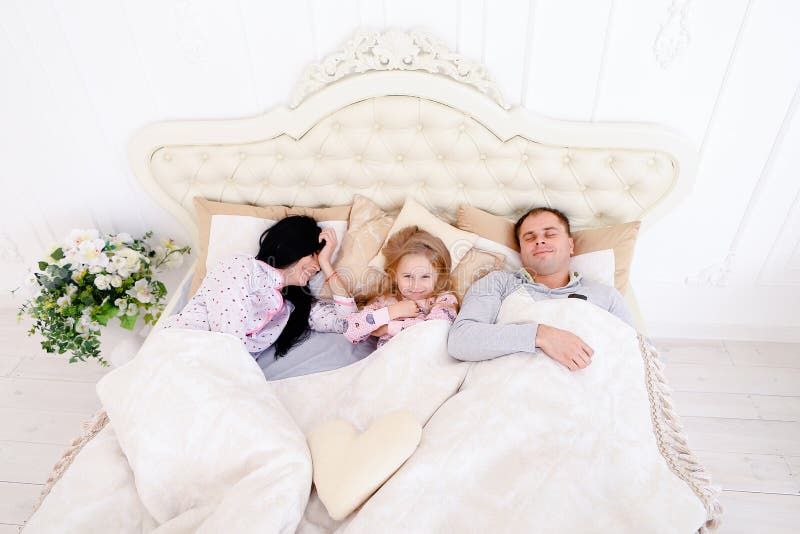 Família feliz que encontra-se em uma cama e em um sono brancos Mãe, pai e imagens de stock Família feliz que encontra-se em uma cama e em um sono brancos Mãe, pai e imagens de stock