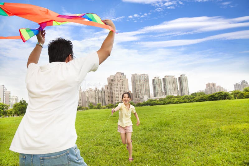 Família feliz que joga o papagaio colorido no parque da cidade imagens de stock Família feliz que joga o papagaio colorido no parque da cidade imagens de stock