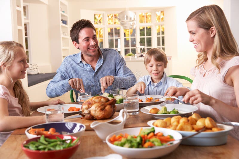 Família feliz que tem o jantar da galinha de assado na tabela