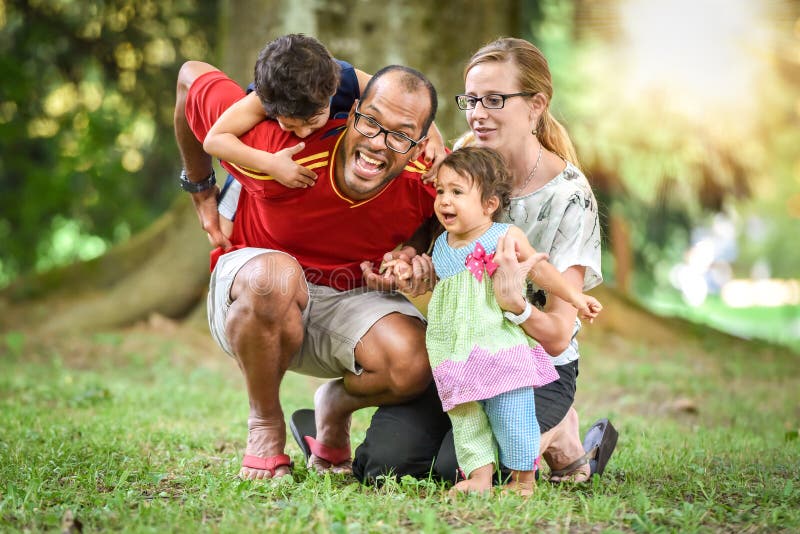 A família inter-racial feliz está sendo ativa um dia no parque imagem de stock A família inter-racial feliz está sendo ativa um dia no parque imagem de stock