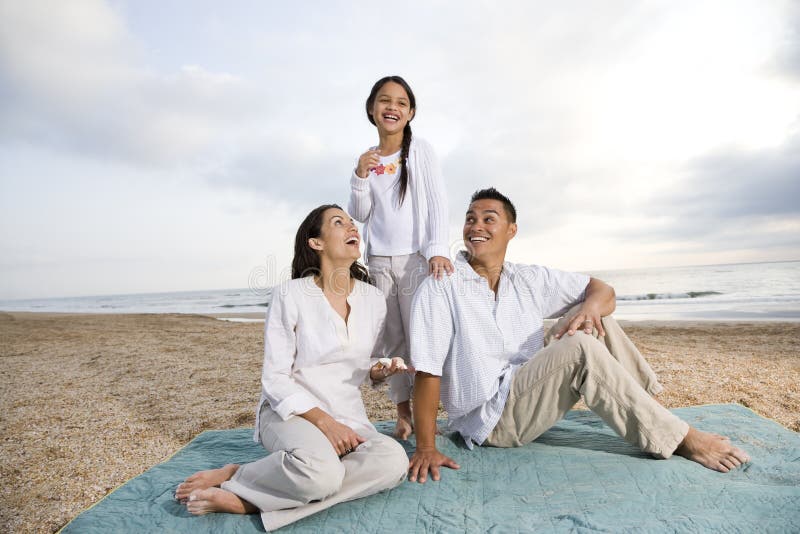 Família latino-americano que senta-se no cobertor na praia