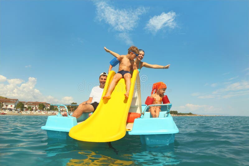 Família no barco do pedal com corrediça amarela no mar