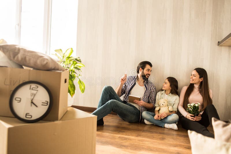 A família nova está sentando-se junto no assoalho na sala de visitas Têm apenas mover-se neste apartamento As meninas são imagem de stock A família nova está sentando-se junto no assoalho na sala de visitas Têm apenas mover-se neste apartamento As meninas são imagem de stock