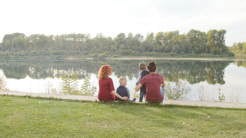 A família nova feliz com dois filhos anda e descansa em um parque pelo rio Família e conceito do relacionamento