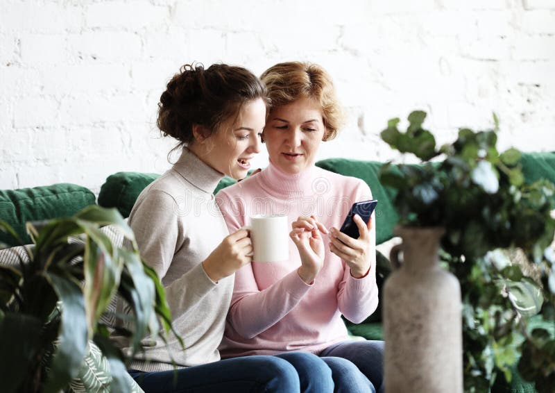 Família, povos e conceito da tecnologia: Mulher envelhecida e sua filha adulta que usa o smartphone em casa foto de stock Família, povos e conceito da tecnologia: Mulher envelhecida e sua filha adulta que usa o smartphone em casa foto de stock