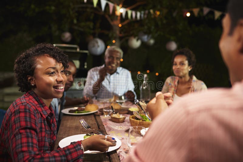 A família preta adulta come o jantar no jardim, sobre a opinião do ombro