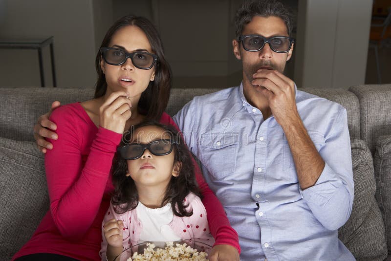 Família que olha a tevê vestir os vidros 3D e comer a pipoca fotografia de stock Família que olha a tevê vestir os vidros 3D e comer a pipoca fotografia de stock