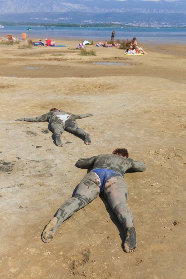 KRK, CROATIA - SEPTEMBER 12, 2011: People smeared with healing mud on beach on September 12, 2011 in Krk, Croatia. Healing mud therapy helps with some skin diseases. KRK, CROATIA - SEPTEMBER 12, 2011: People smeared with healing mud on beach on September 12, 2011 in Krk, Croatia. Healing mud therapy helps with some skin diseases.